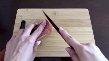 Kadın eli, ahşap bir tahtanın üzerinde siyah bir bıçakla tütsülenmiş sosis kesiyor.