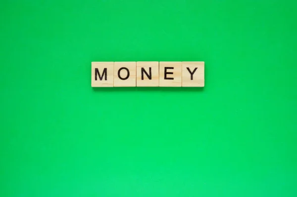 お金だ 緑の背景の上にレタリングと木製のブロック 緑の表面に文字を持つ木製のブロックのトップビュー — ストック写真
