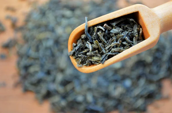 Wooden spoon with loose leaf tea on blurred heap of tea background