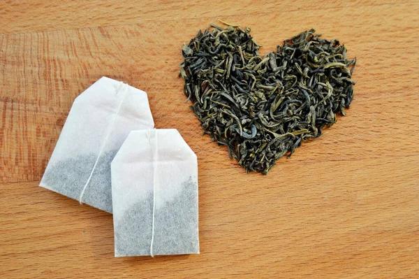 Heart made from loose leaf tea and tea bags on wooden background
