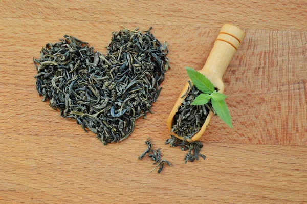 Heart made from loose leaf tea and wooden spoon with fresh mint leaves on wooden background