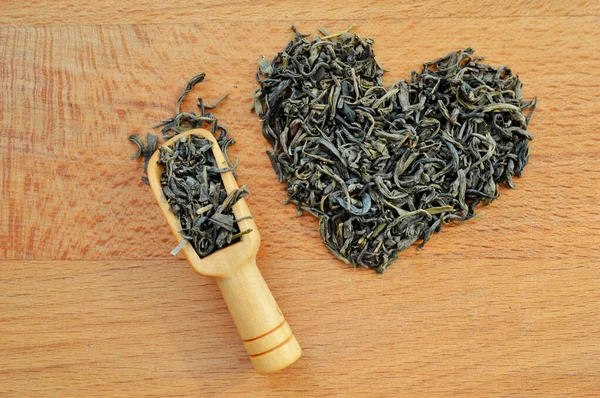 Kırık yapraklı çay ve ahşap arka planda tahta kaşıktan yapılmış bir kalp.