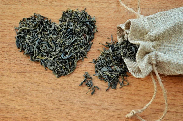 Heart made of loose leaf tea and jute bag on wooden background