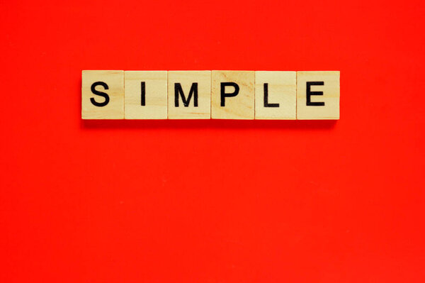 Word simple. Wooden blocks with lettering on top of red background. Top view of wooden blocks with letters on red surface