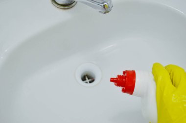 Lastik sarısı eldivendeki bir el deterjanı tutar ve lavaboyu yıkar.
