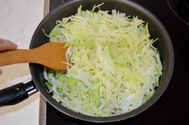 Tavada haşlanmış lahana, ahşap bir spatulayla karıştırılır.