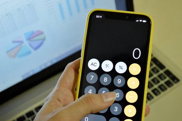 Telefondaki hesap makinesi bilgisayarın arka planında grafikle birlikte.
