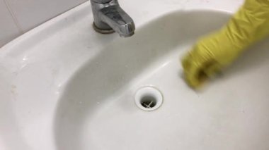 Kauçuk sarısı bir eldiven ile lavaboyu süngerle yıkar..