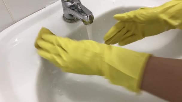 La mano en un guante amarillo de goma lava el fregadero con una esponja. — Vídeo de stock