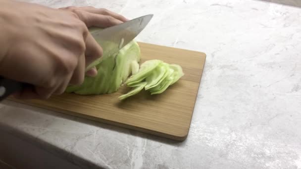 Chica corta una cabeza verde de col con un cuchillo en una tabla. — Vídeo de stock