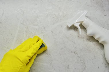 Lastik eldivenli bir el ve sarı bir eldiven fayansları süngerle yıkar.