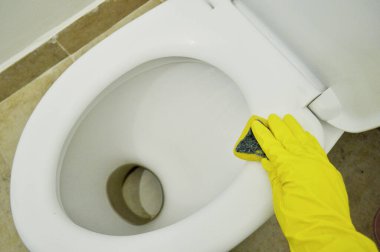 Kauçuk sarısı bir eldiven ile tuvaleti süngerle yıkar.