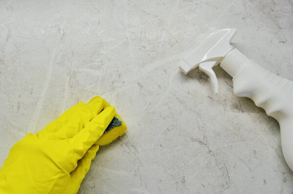 Рука в резиновой перчатке и жёлтой перчатке моет плитку губкой