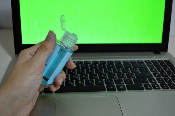 Antiseptikum in der Hand auf dem Hintergrund eines Laptops mit grünem Bildschirm — Stockbild Antiseptikum Der Hand Auf Dem Hintergrund Eines Laptops Mit Grünem — Stockfoto