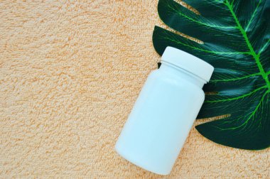 Beyaz kavanoz, bir palmiye yaprağının üzerinde bej kumaşın arka planında duruyor.