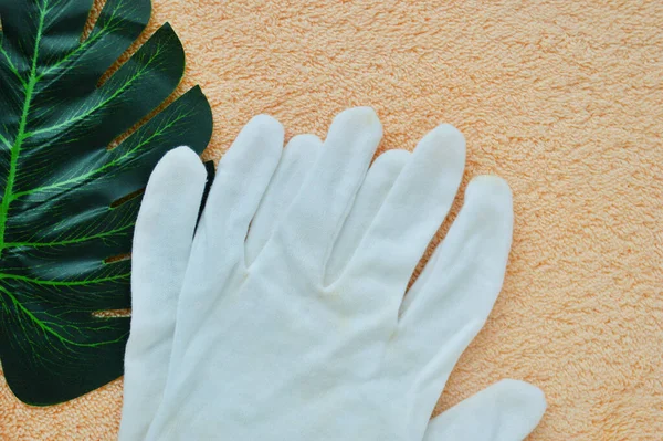 Guantes de tela blanca se encuentran en una hoja de palma sobre un fondo de tela beige. —  Fotos de Stock
