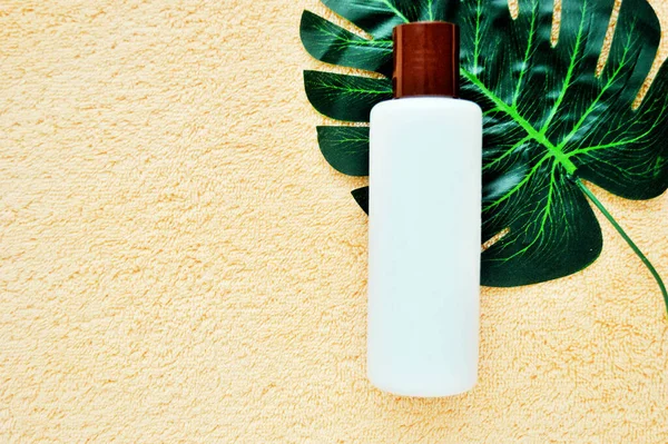 Weiße Plastikflasche liegt auf einem Palmblatt auf einem beigen Stoffhintergrund — Stockfoto