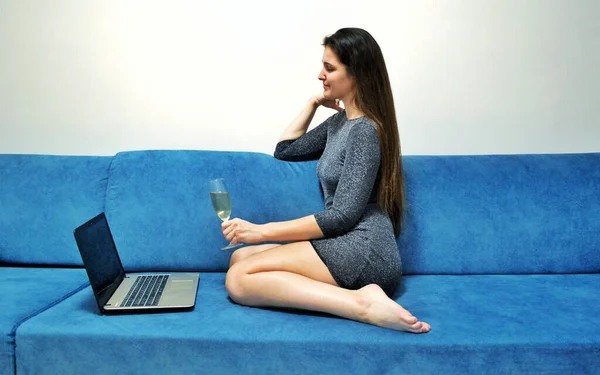 Девушка сидит в платье с бокалом шампанского в руках перед ноутбуком — стоковое фото