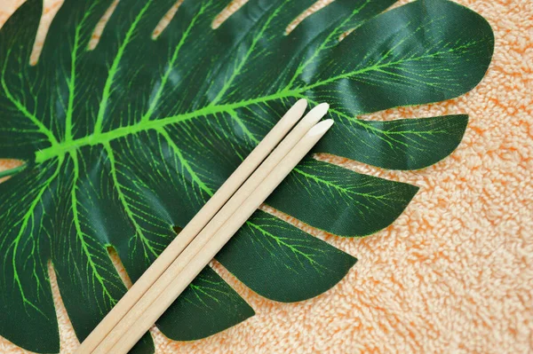 Wooden sticks for manicure lie on a palm leaf on a background of beige fabric.