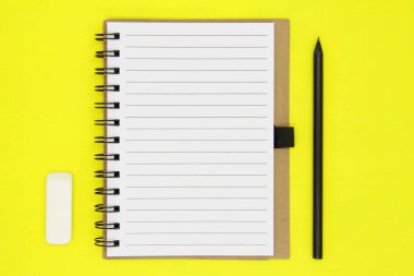 Okula dönelim. Eğitim konsepti, ofis malzemeleri. Craft Notepad, izole edilmiş sarı arka planda siyah kalem ve beyaz silgi. Uzayı kopyala Dümdüz. Yukarıdan görünüşü.