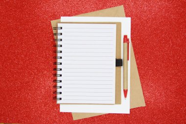 Not Defteri 'nde ofis aksesuarlarıyla yeni yıl hedefi, planı, aksiyon metni. İş motivasyonu, ilham kavramları. Not defteri ve kalem, parlak kırmızı arka planda bir zarf. Dümdüz. Yukarıdan görünüşü.