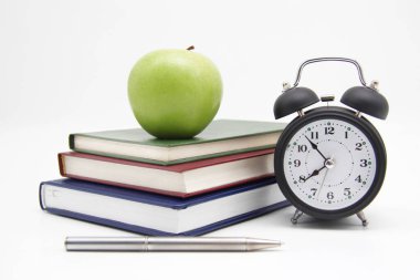 Okula dönelim. Eğitim konsepti, ofis malzemeleri. Bir yığın kitap, yeşil bir elma, bir çalar saat ve izole edilmiş beyaz arka planda bir kalem. Boşluğun bir kopyası.