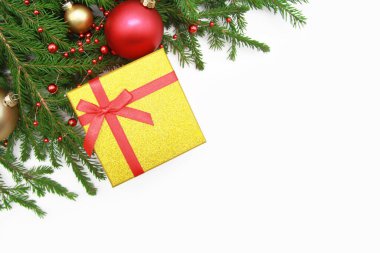 Şenlik nitelikleriyle yeni yıl kompozisyonu. Kırmızı fiyonklu altın hediye kutusu, köknar dalları, altın ve kırmızı Noel topları, beyaz arka planda boncuklar. Dümdüz. Yukarıdan manzara. Kopyalama alanı.