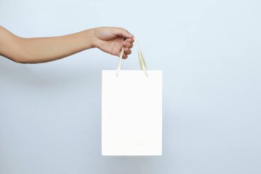Bir el, çevrimiçi yiyecek ve hediye paketi için beyaz bir arka planda fotokopi alanı olan kağıt beyaz bir poşet tutuyor. Restoran ve mağazada kurye işi konsepti.