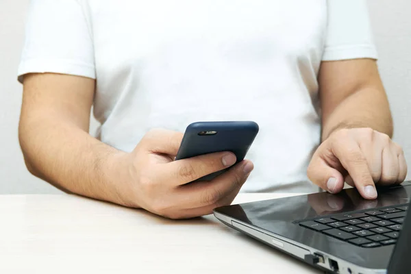 A person is holding a phone and working with a laptop at a table with copy space. Concept of lifestyle business and mobile Internet technologies in the office