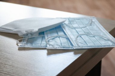 Masanın kenarında iki yeni koruyucu mavi tıbbi yüz maskesi. Viral enfeksiyon salgını sırasında güvenlik ve önleme kavramı COVID-19