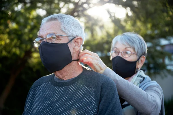 Active senior couple on outdoor walk wearing face masks. Woman helping man with mask.