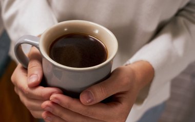 Süveter giyen bir kadının elinde bir fincan sıcak kahve tutarken yakın plan fotoğrafı.