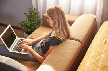 Oturma odasındaki kanepede çalışan genç bir kadın.