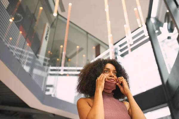 African woman putting on face mask before leaving office.