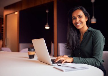 İş kadını portresi toplantı masasında oturmuş bilgisayarla modern açık planlama ofisinde çalışıyor.