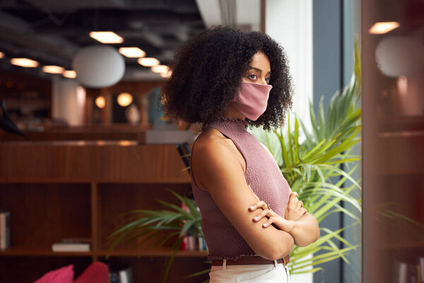 Деловая женщина в маске для лица в современном офисе открытого плана во время пандемии Ковид-19