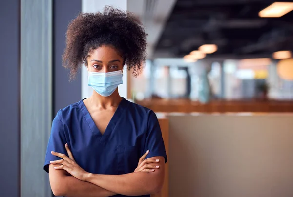 Female Doctor In Face Mask Wearing Scrubs Under Pressure In Busy Hospital During Health Pandemic