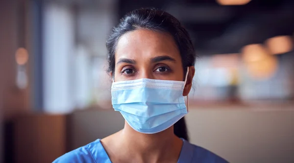 Female Doctor In Face Mask Wearing Scrubs Under Pressure In Busy Hospital During Health Pandemic