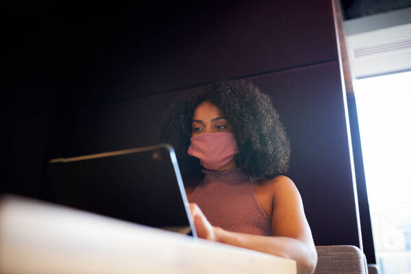 Деловая женщина в маске, работающая в социально отдаленной кабинке во время пандемии здоровья