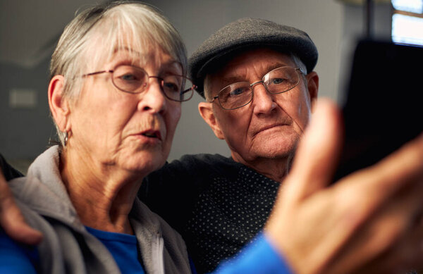 Senior Couple At Home Making Video Call To Family On Mobile Phone