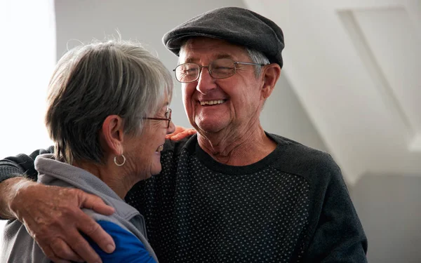 Loving Senior Couple Laughing And Smiling As They Hug Each Other At Home Together
