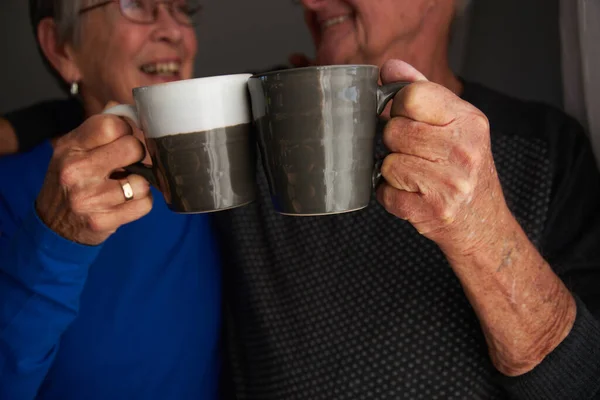 Smiling Senior Couple Making Cheers With Cups At They Real With Hot Drink At Home