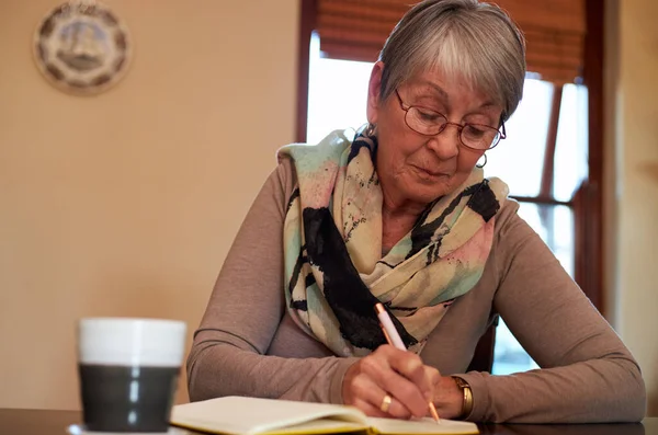 Mulher Sênior Casa Sentada Mesa Escrevendo Caderno Jornal — Fotografia de Stock