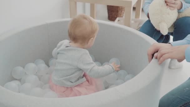 Vackra lilla tjej sits i poolen med bollar och spela. Slow motion — Stockvideo