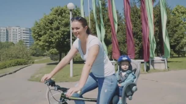 Счастливая мать со своим маленьким сыном едут на велосипеде в парк. Медленное движение — стоковое видео