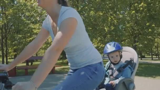 Madre feliz con su hijo pequeño están montando una bicicleta en el parque. Movimiento lento — Vídeos de Stock