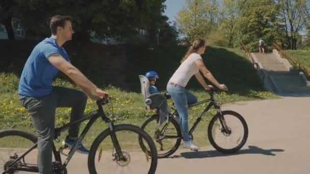 Familia feliz con su hijo pequeño están montando una bicicleta en el parque. Movimiento lento — Vídeo de stock