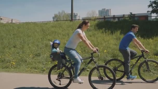 Familia feliz con su hijo pequeño están montando una bicicleta en el parque. Movimiento lento — Vídeo de stock