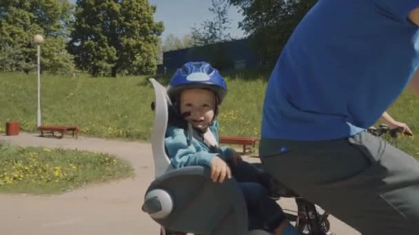 Joven más lejos con su pequeño hijo están montando una bicicleta en el parque. Movimiento lento — Vídeo de stock