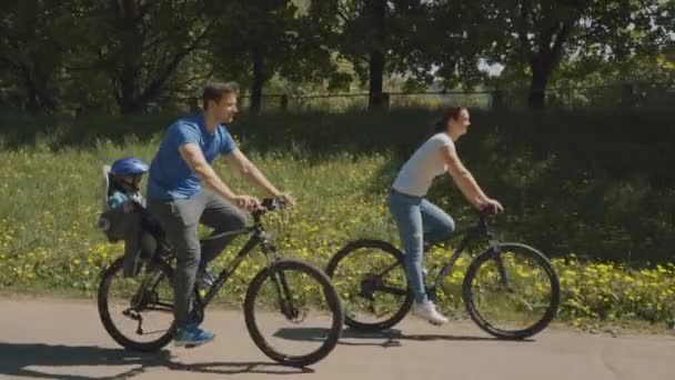 Familia feliz con su hijo pequeño están montando una bicicleta en el parque. Movimiento lento — Vídeos de Stock